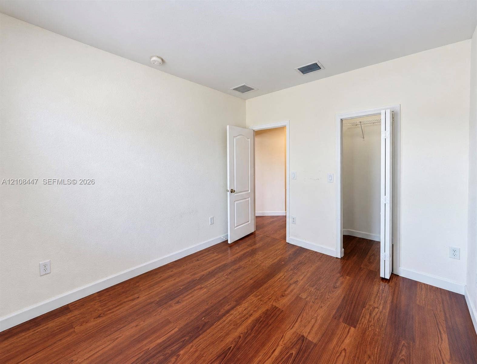 Room featuring wood-finish flooring, neutral wall paint, a six-panel interior door, and a built-in closet with bifold doors