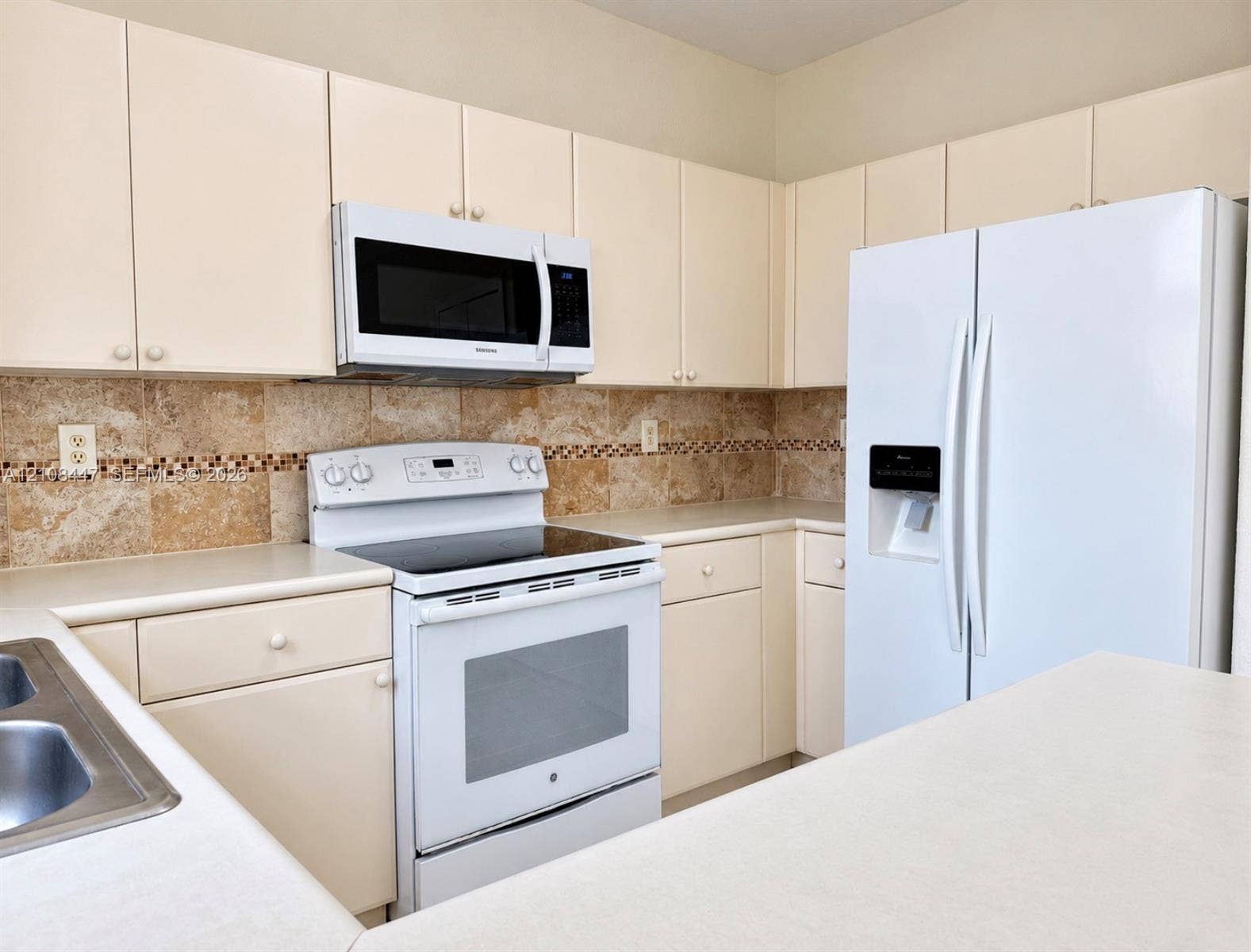 Kitchen featuring white cabinetry, solid surface countertops, a natural stone tile backsplash with a decorative mosaic border, and white appliances
