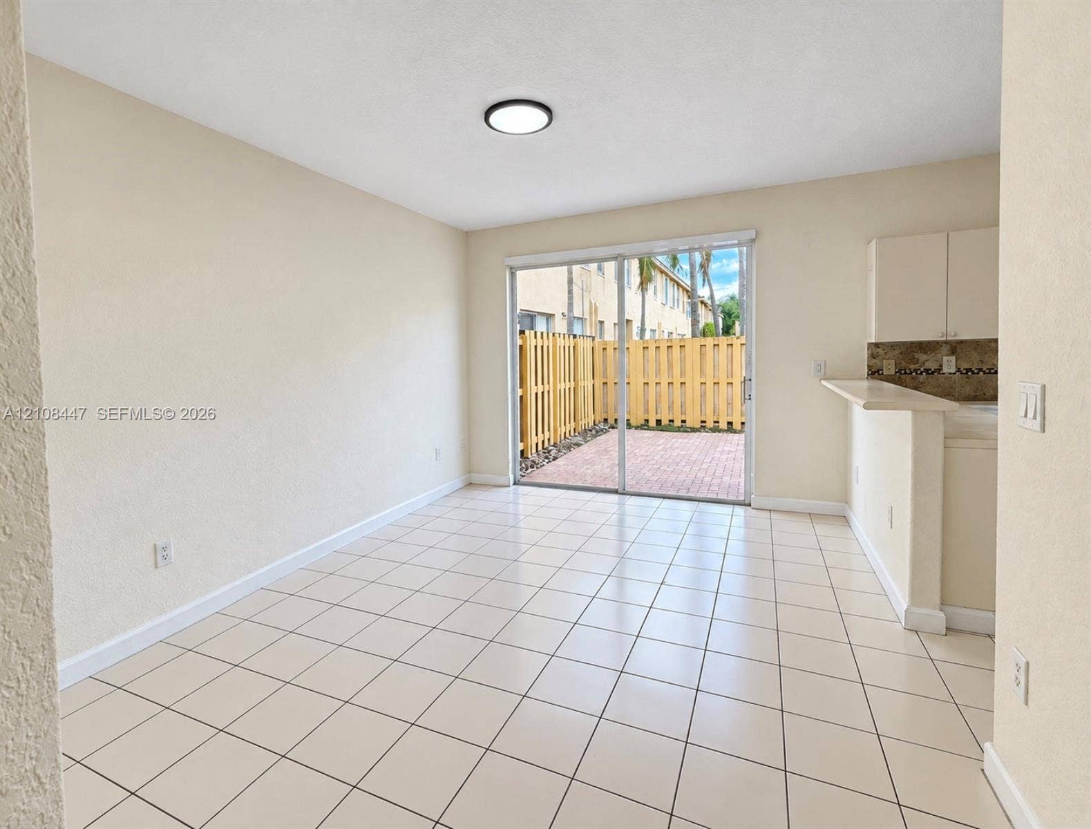 Neutral-toned interior featuring ceramic tile flooring, a breakfast bar, and sliding glass doors opening to a private, fenced brick patio
