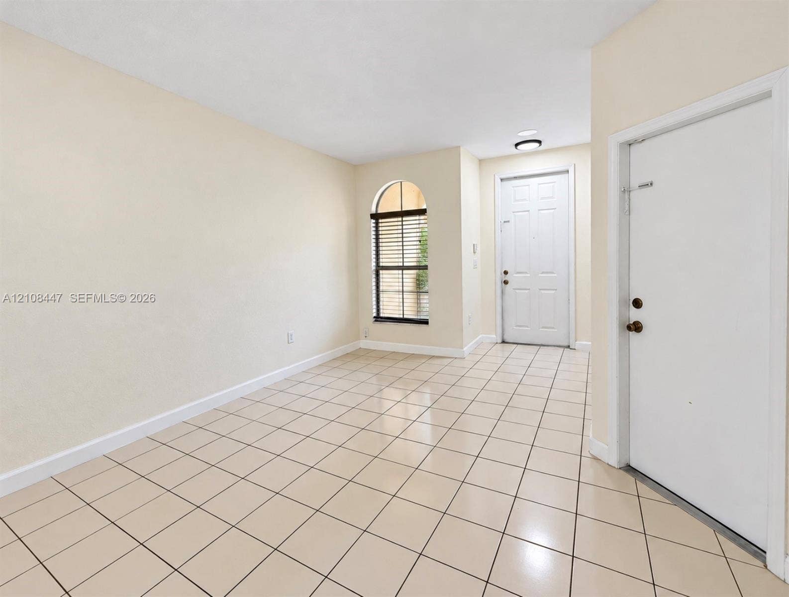 Interior area featuring neutral-toned floor tiling, an arched window, a paneled front entry door, and a recessed ceiling light fixture