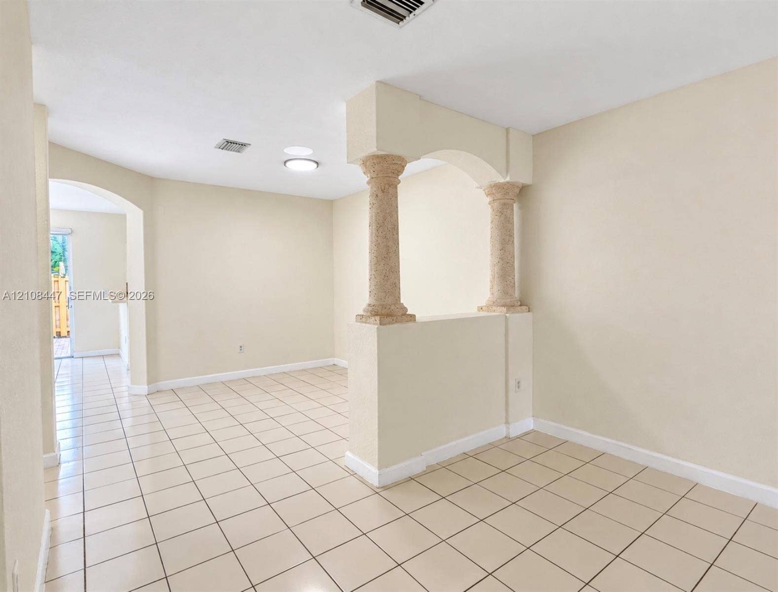Interior space featuring neutral wall tones, ceramic tile flooring, textured stone-style pillars, and arched structural detailing