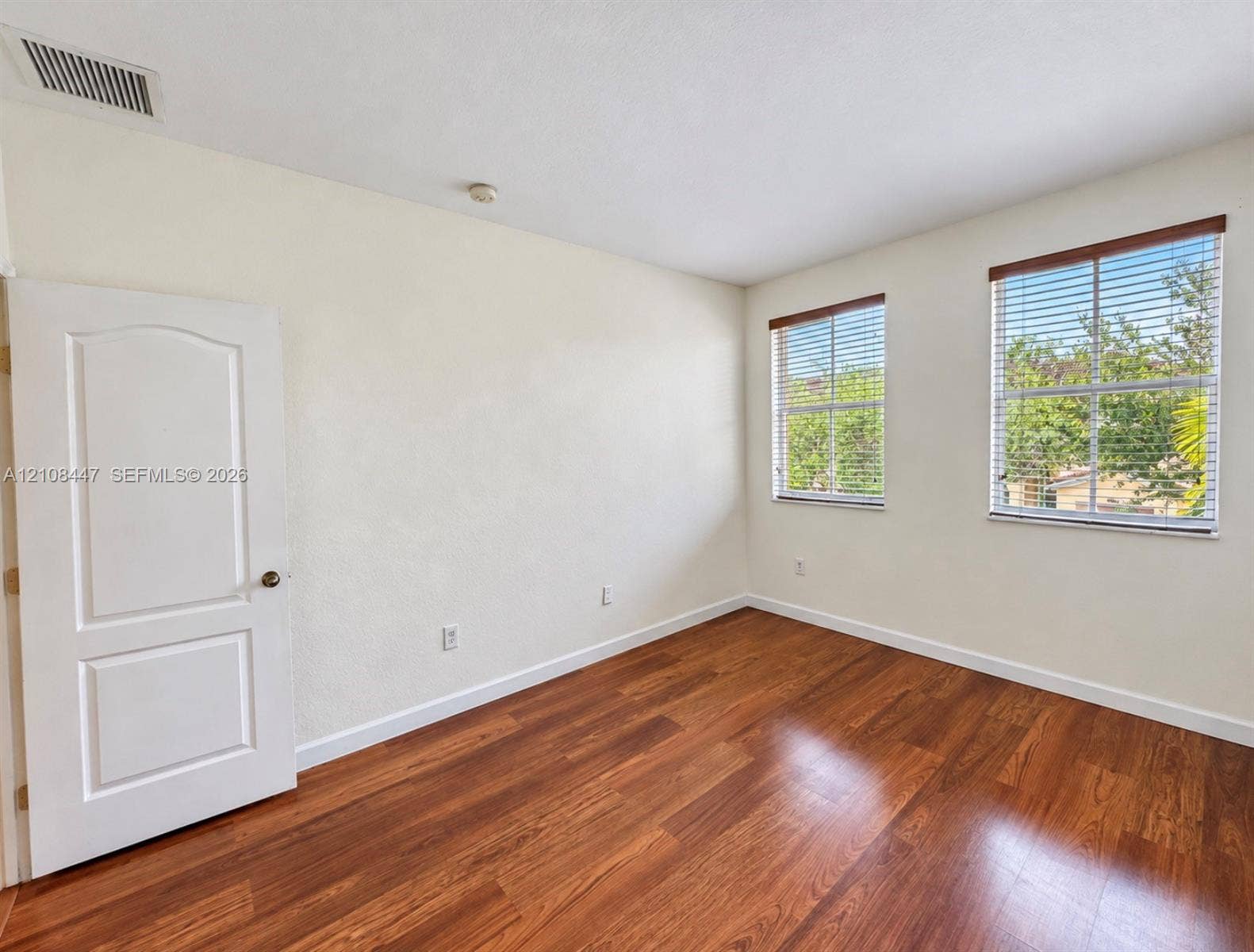 Room featuring wood-finish flooring, two windows with horizontal blinds, and a two-panel interior door