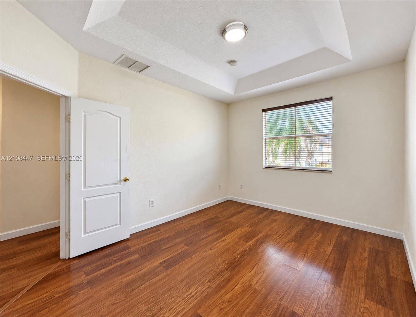Room featuring a tray ceiling, wood-finish flooring, and a window with horizontal blinds