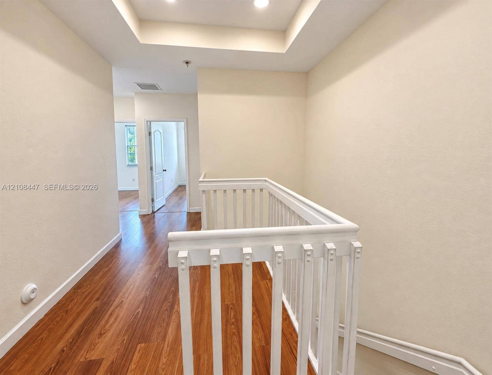 Tray ceiling featuring recessed lighting, wood-finish flooring, and white painted balustrade railing