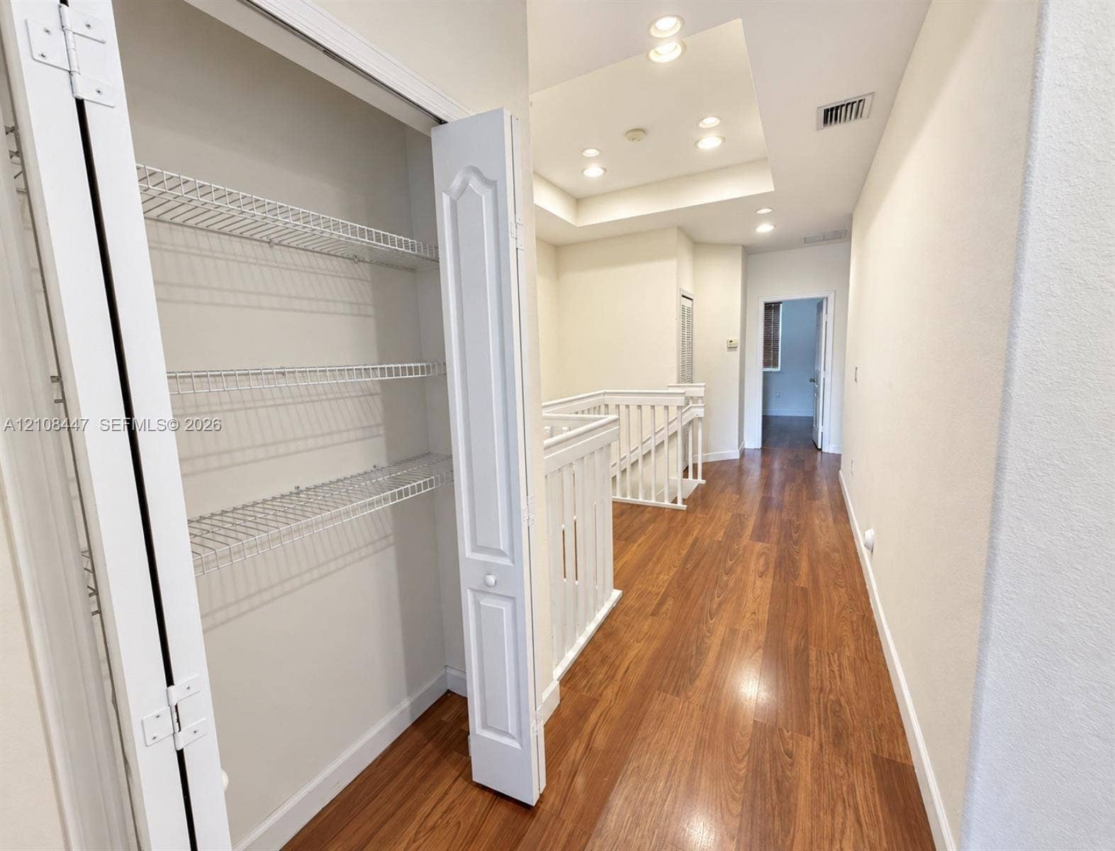 Hallway featuring wood-finish flooring, recessed ceiling lighting, a recessed tray ceiling, and a closet with white bi-fold doors and wire shelving