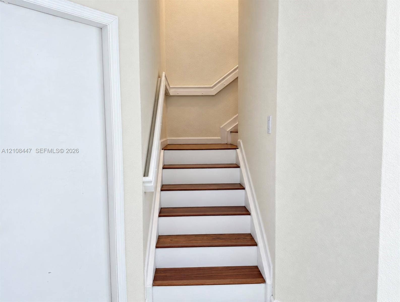 Staircase featuring wood-finish treads, white risers, and a continuous wall-mounted handrail