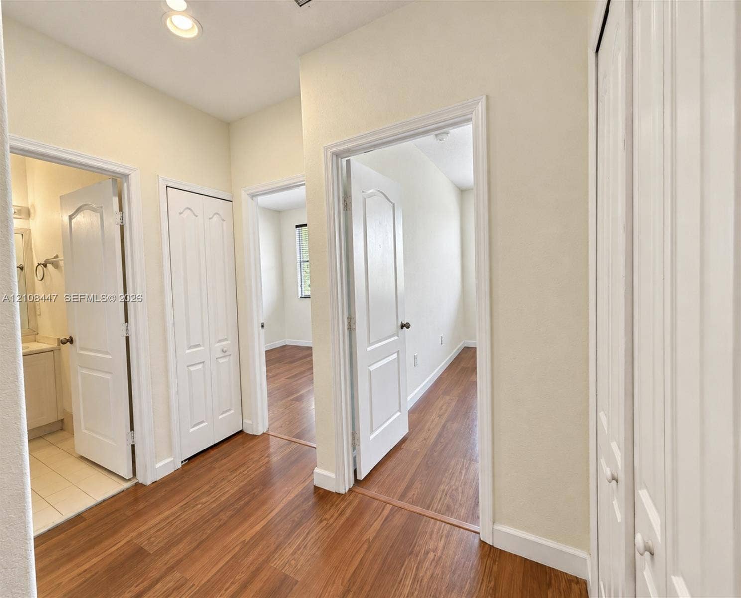 Hallway featuring wood-finish flooring, white paneled interior doors, and multiple built-in closets with bi-fold doors