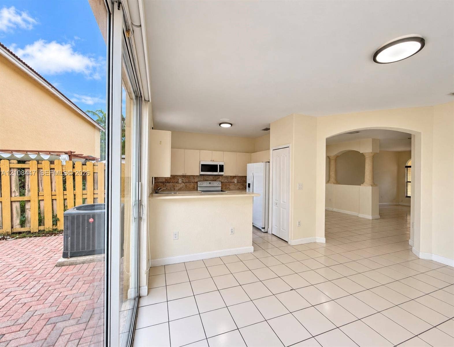 Kitchen featuring a breakfast bar, stone-finish backsplash, and built-in cabinetry, with ceramic tile flooring and sliding glass doors opening to a brick-paved patio