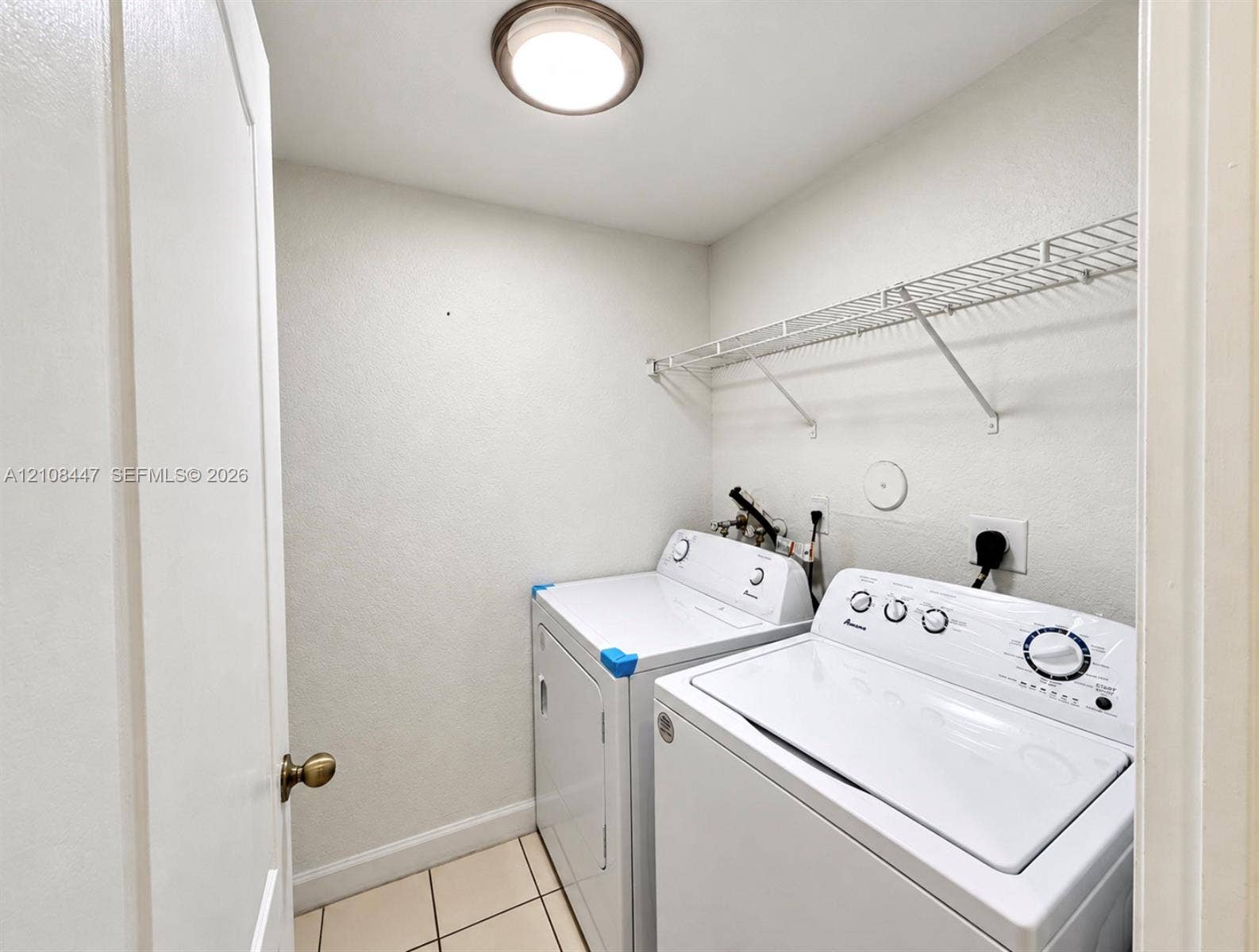 Utility area featuring ceramic tile flooring, a wall-mounted wire storage shelf, and a flush-mount overhead light fixture