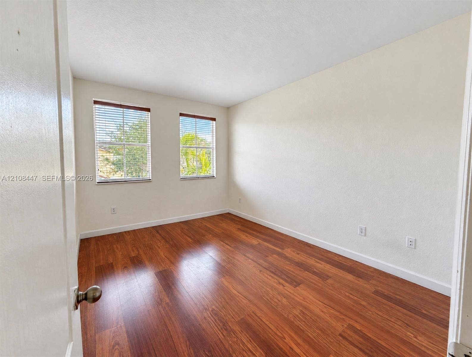 Room featuring wood-finish flooring, neutral walls, and two double-hung windows with installed blinds