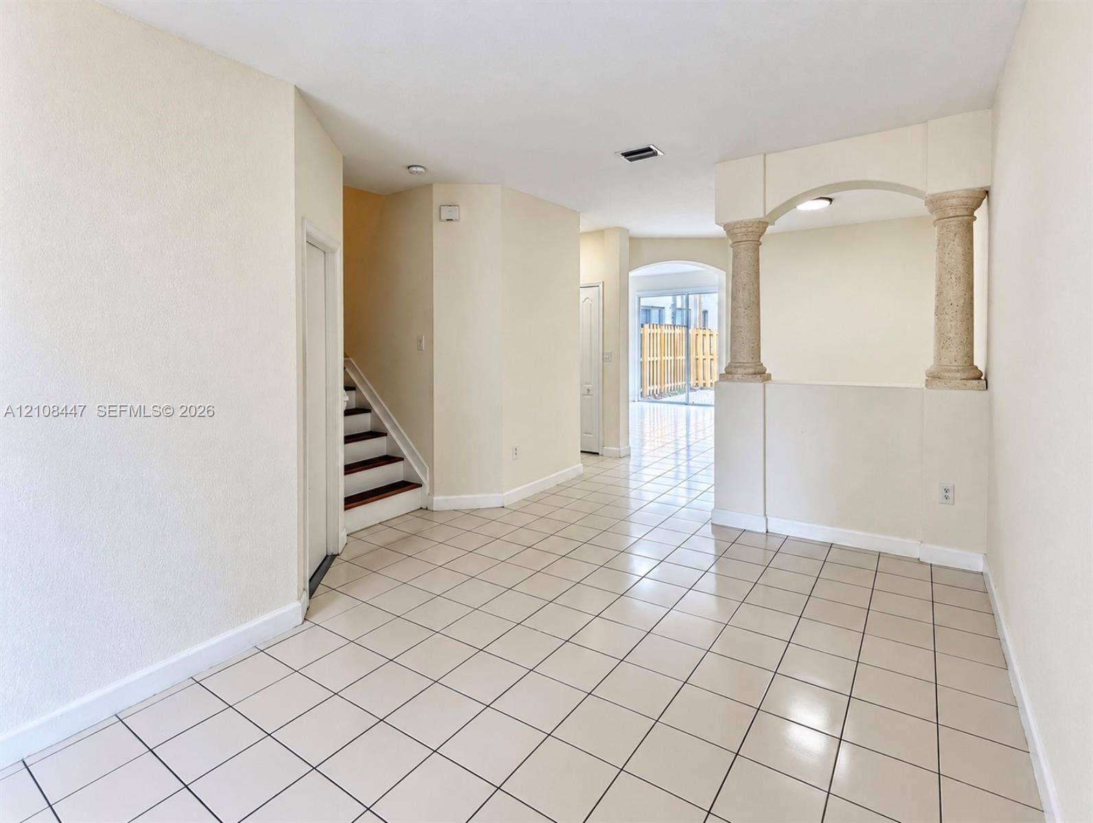 Interior featuring ceramic tile flooring, decorative structural columns with arched alcove, and a staircase with wood-finish treads