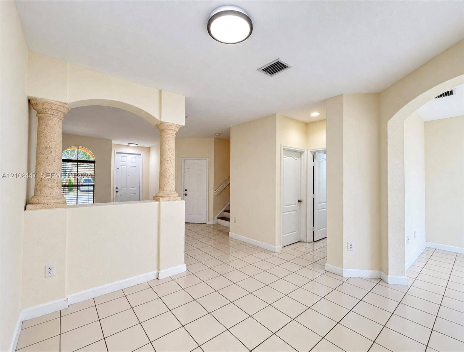 Interior space featuring light-colored tile flooring, decorative stone-finish columns, arched wall openings, and recessed ceiling lighting