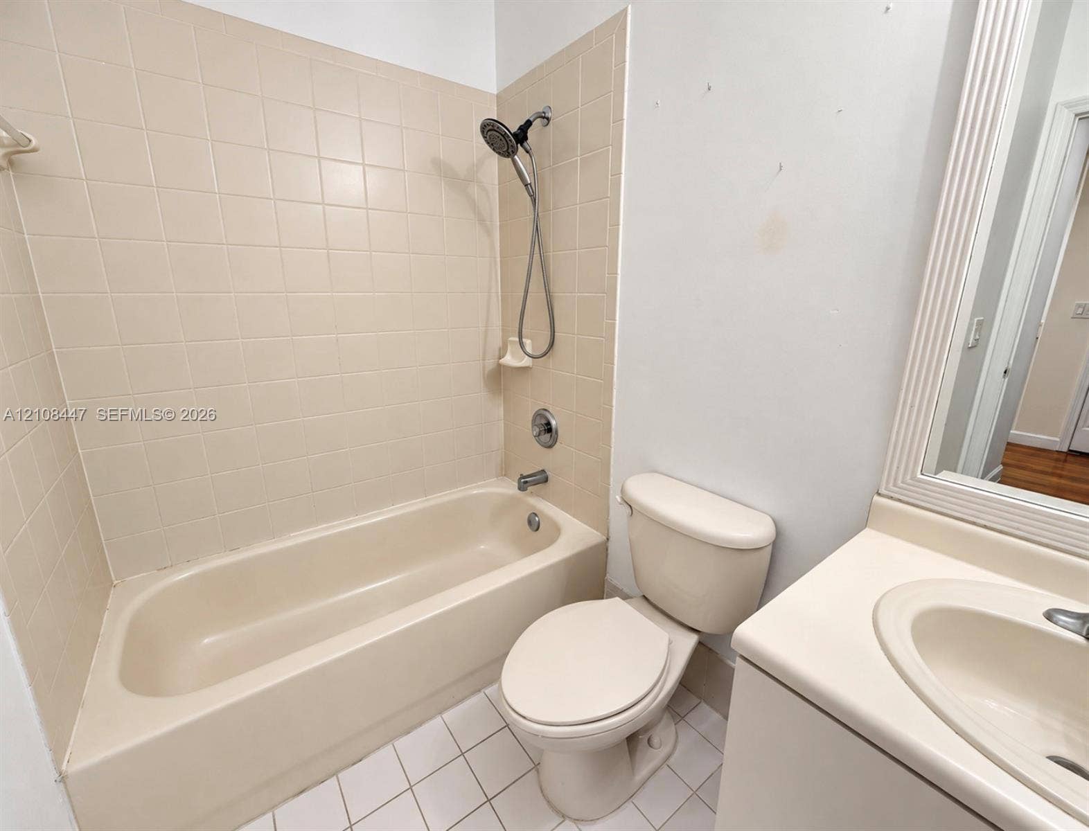 Full bathroom featuring a tub-shower combination with ceramic tile surround, a porcelain toilet, and a vanity with an integrated basin and framed wall mirror