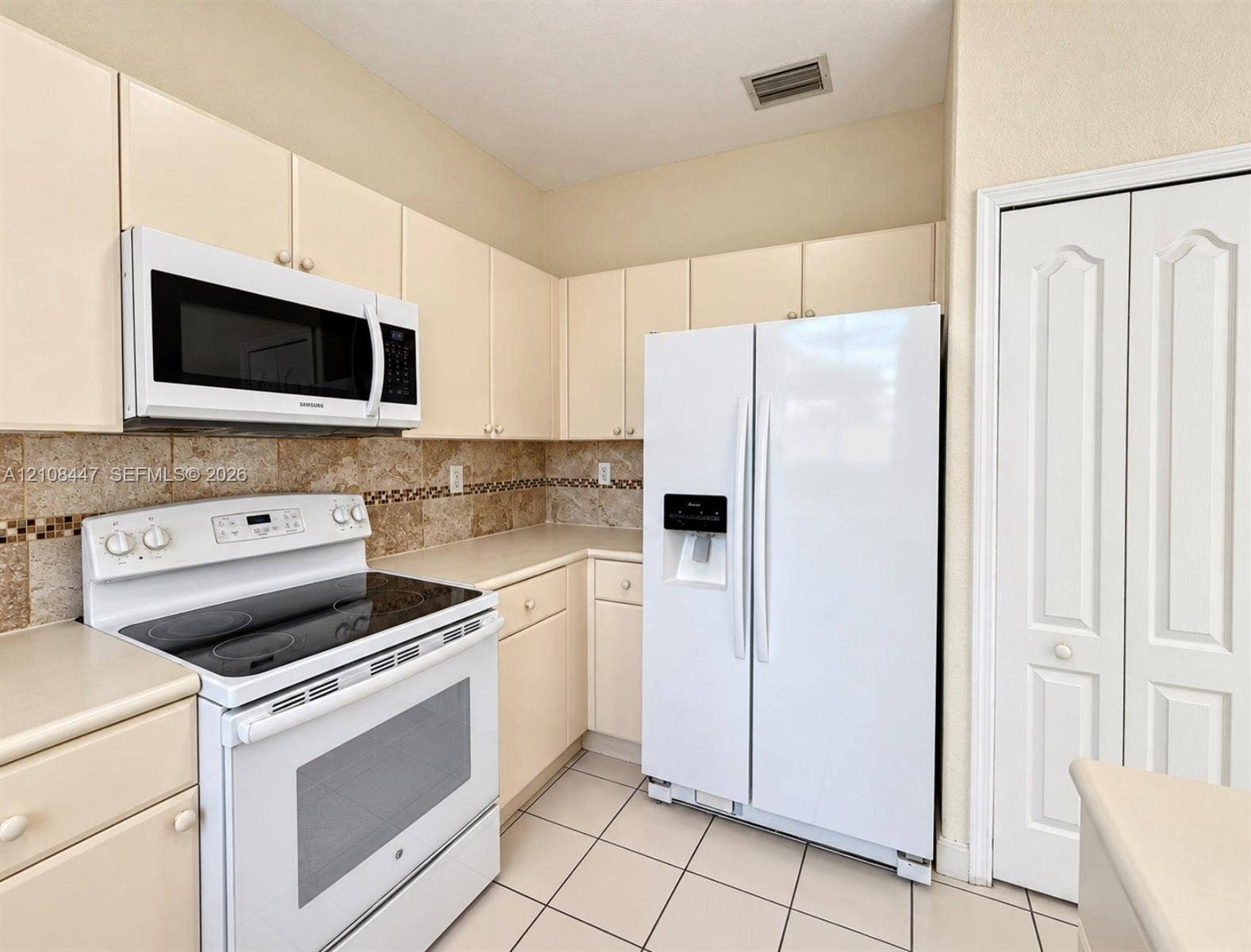 Kitchen featuring solid-surface countertops, stone tile backsplash with decorative inlay, white appliances, and light-toned cabinetry