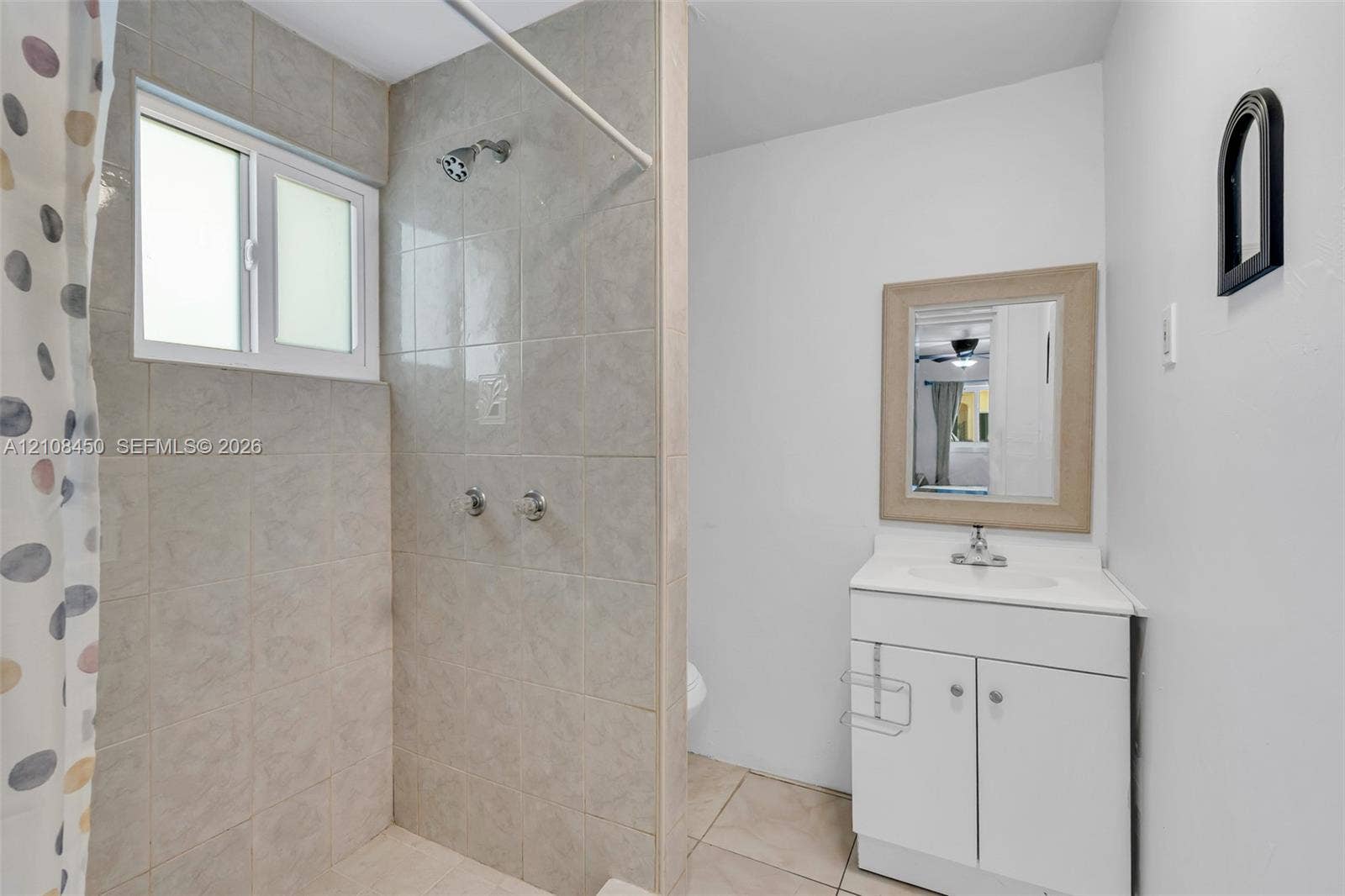 Bathroom featuring tile-surround shower, white vanity cabinet with integrated sink, rectangular wall-mounted mirror, and tile flooring