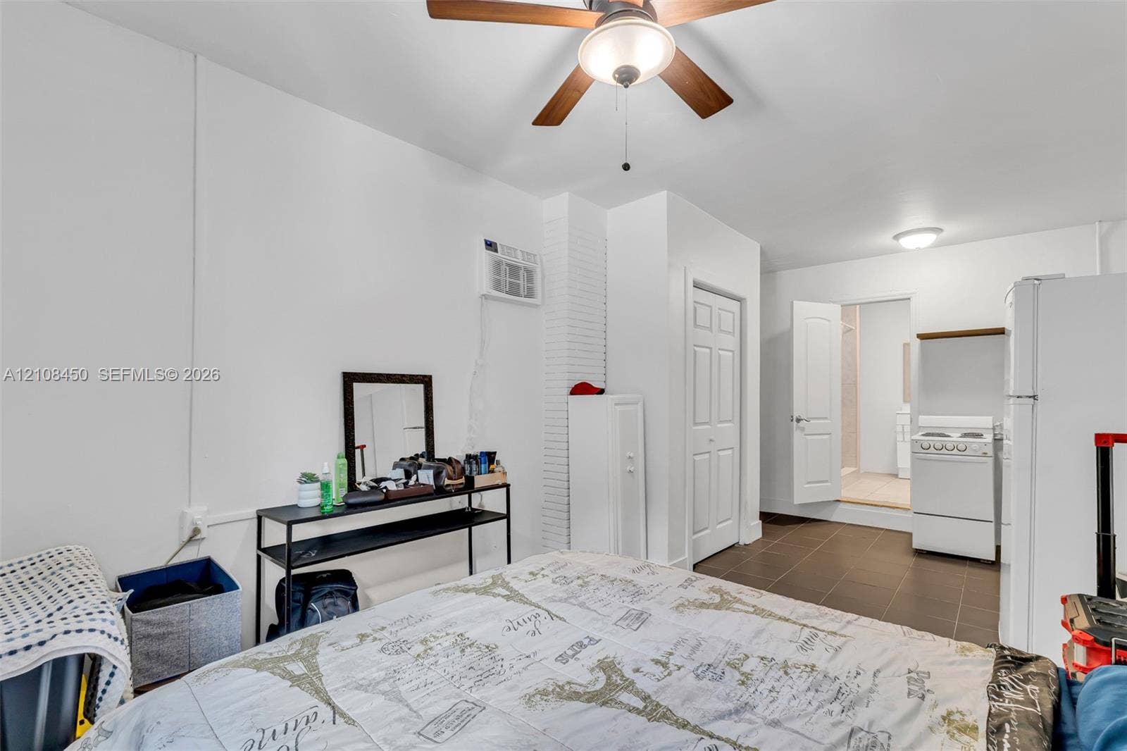 Room featuring white walls, a ceiling fan with integrated lighting, dark tile flooring, a wall-mounted cooling unit, and a built-in pantry