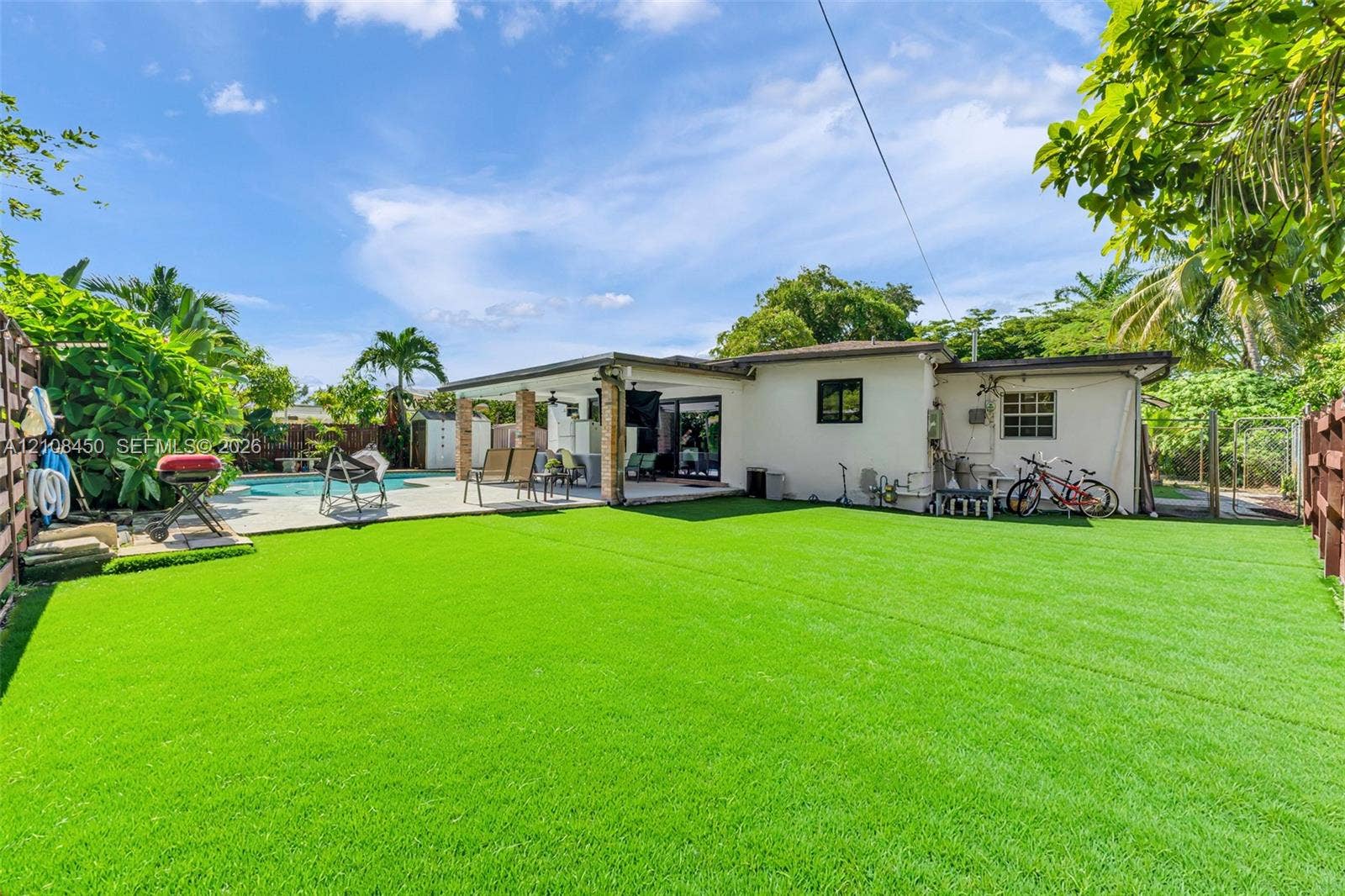 Expansive backyard featuring synthetic turf, a concrete patio, a covered lanai, an in-ground swimming pool, and wood-paneled privacy fencing