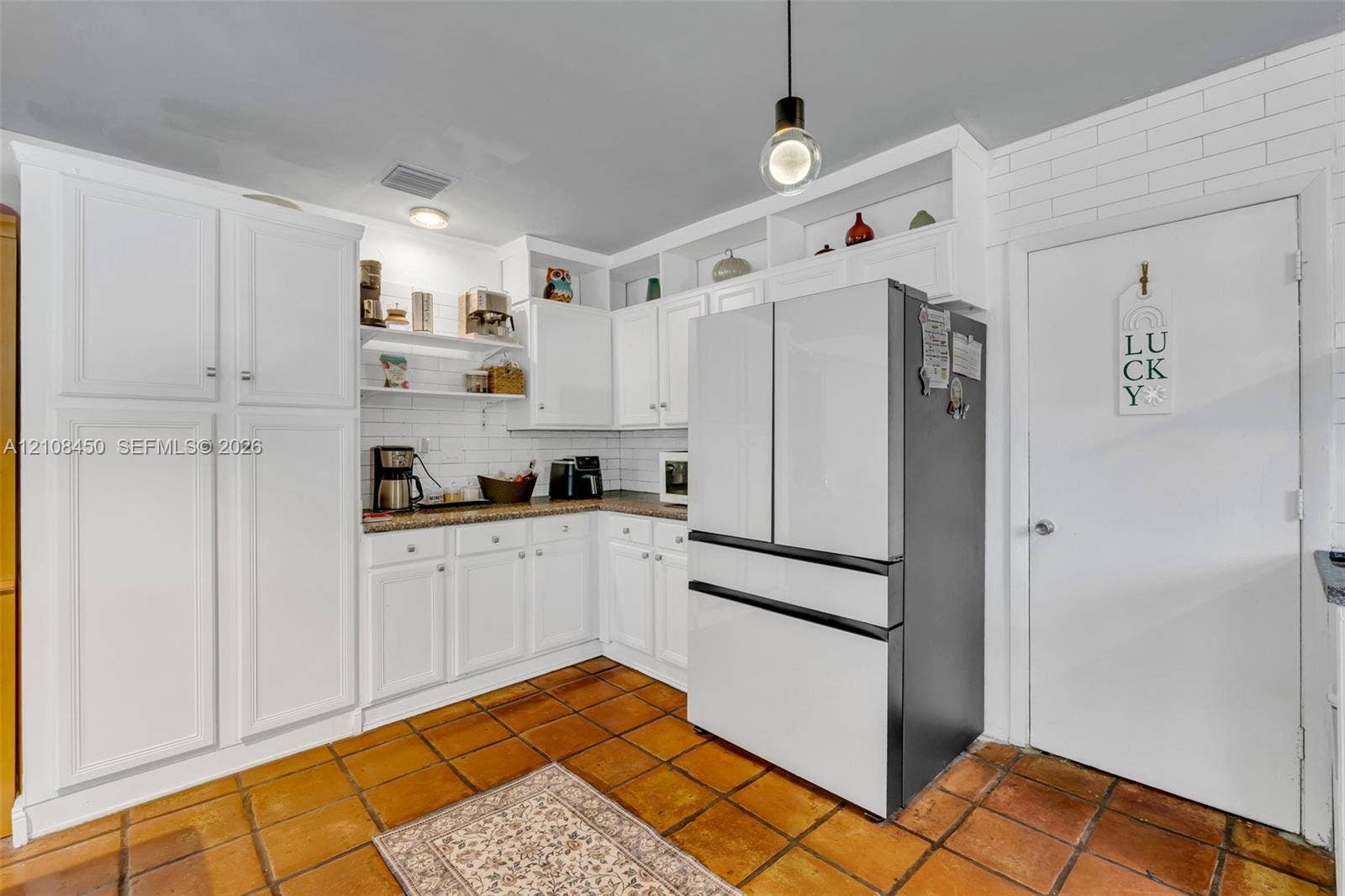 White cabinetry with built-in open shelving, subway tile backsplash, multi-tone countertop, and terracotta tile flooring