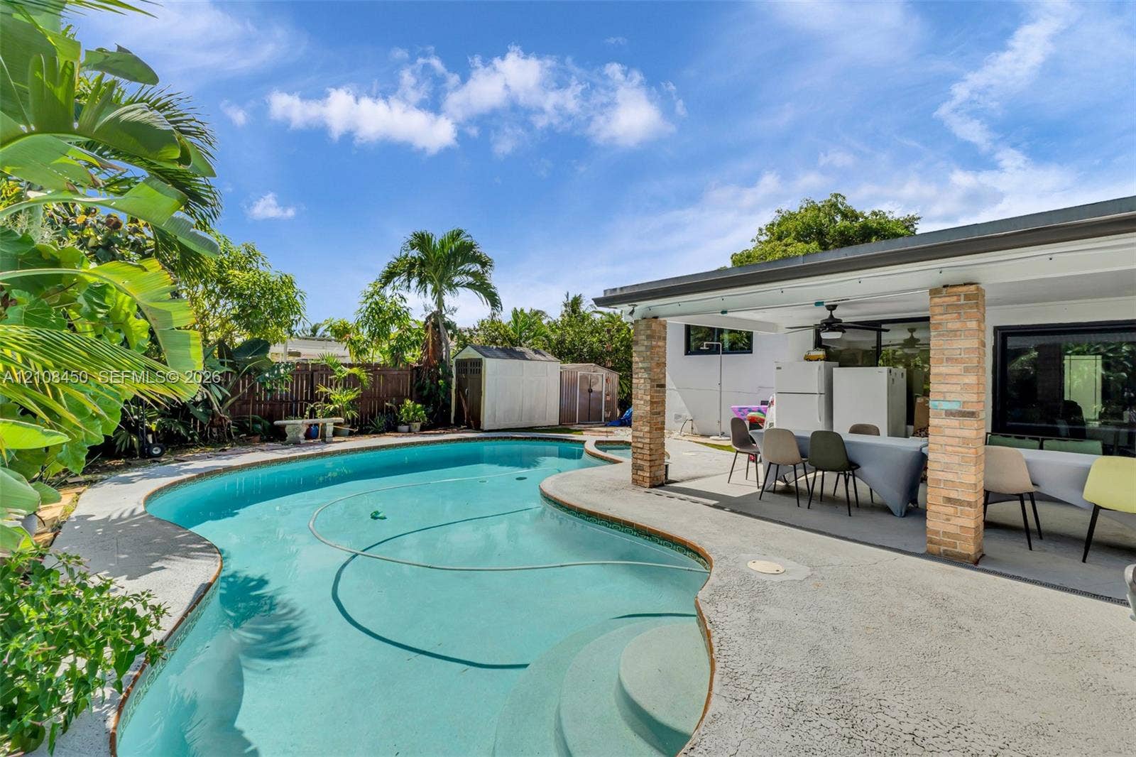 Free-form inground pool with built-in stairs, expansive concrete patio, and brick-columned covered porch
