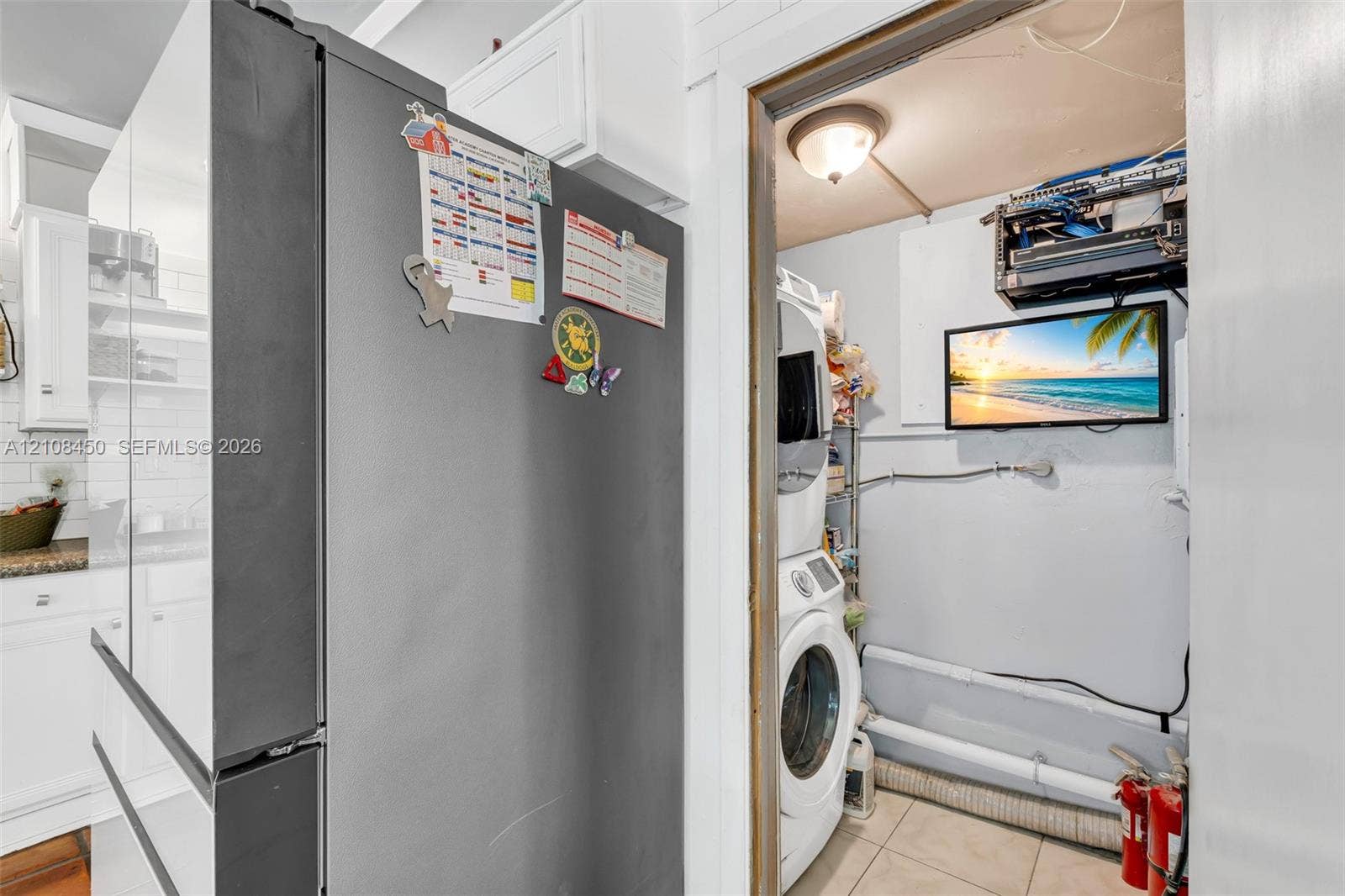 Kitchen featuring a stainless steel refrigerator and white cabinetry with subway tile backsplash, inclusive of a utility area with a stacked washer and dryer unit