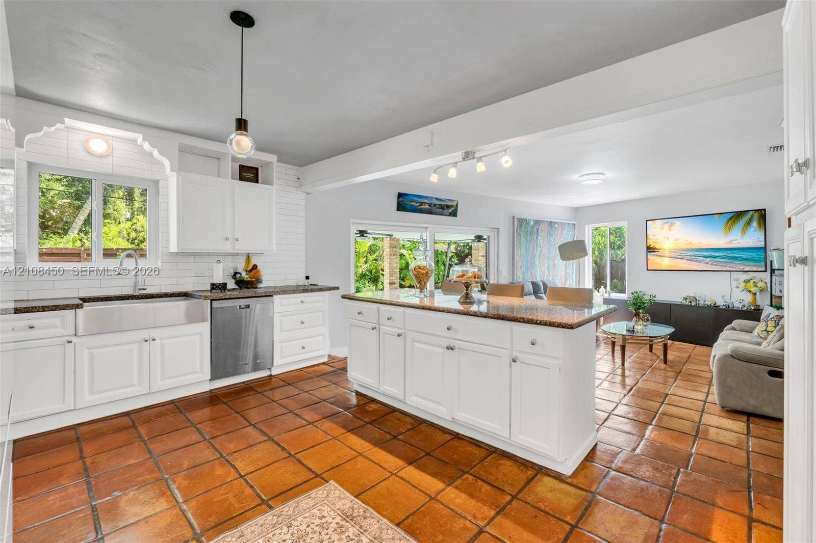 Kitchen featuring white cabinetry, a farmhouse-style stainless steel apron sink, a central island with a stone-finish countertop, white subway tile backsplash, and terracotta tile flooring