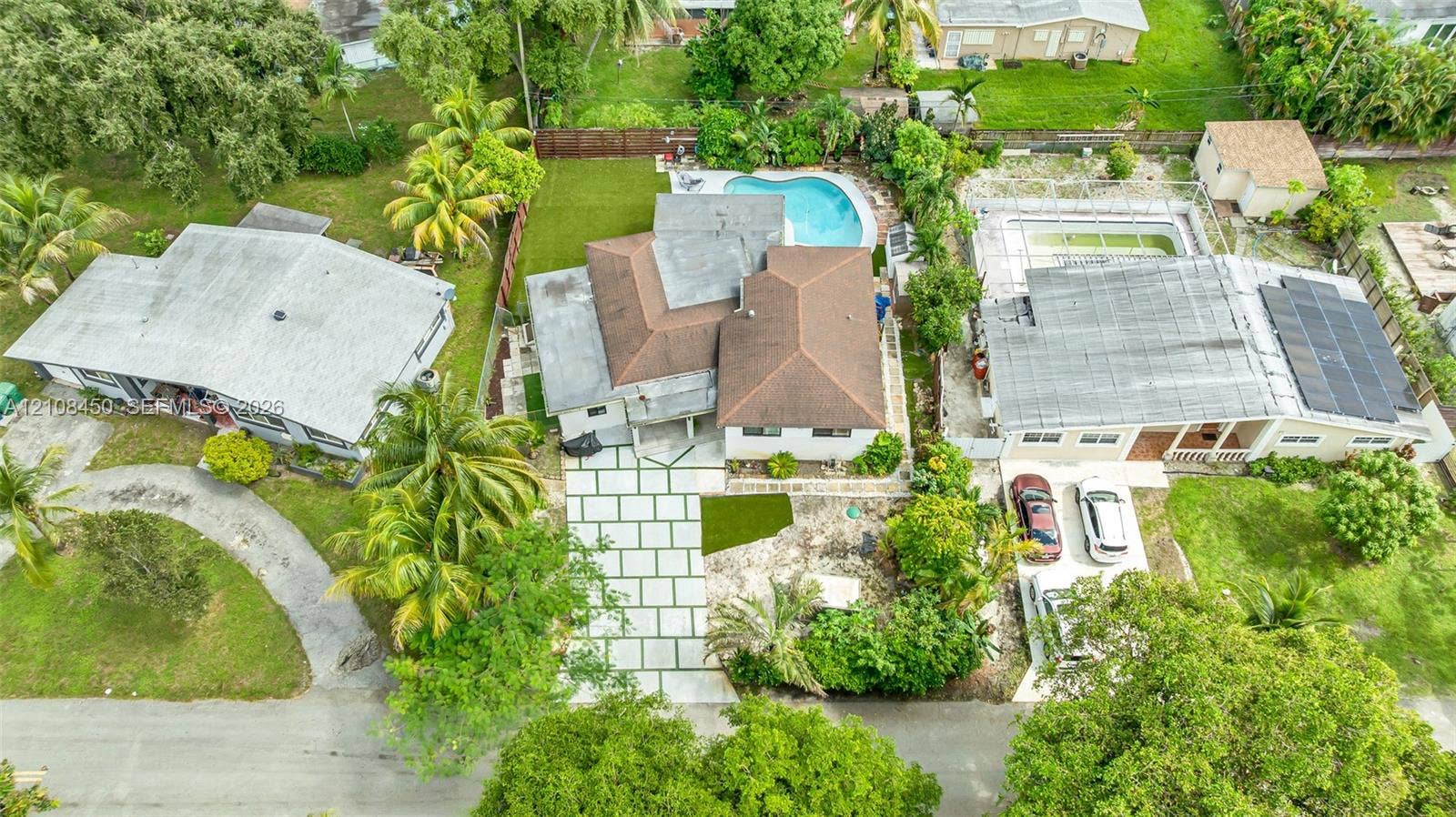 Aerial perspective of a property featuring a multi-pitched roof, paver driveway, swimming pool, and manicured lawn