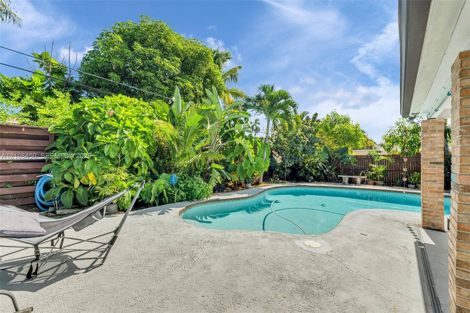 Outdoor swimming pool with curved concrete decking, horizontal slat wood fencing, and mature tropical landscaping