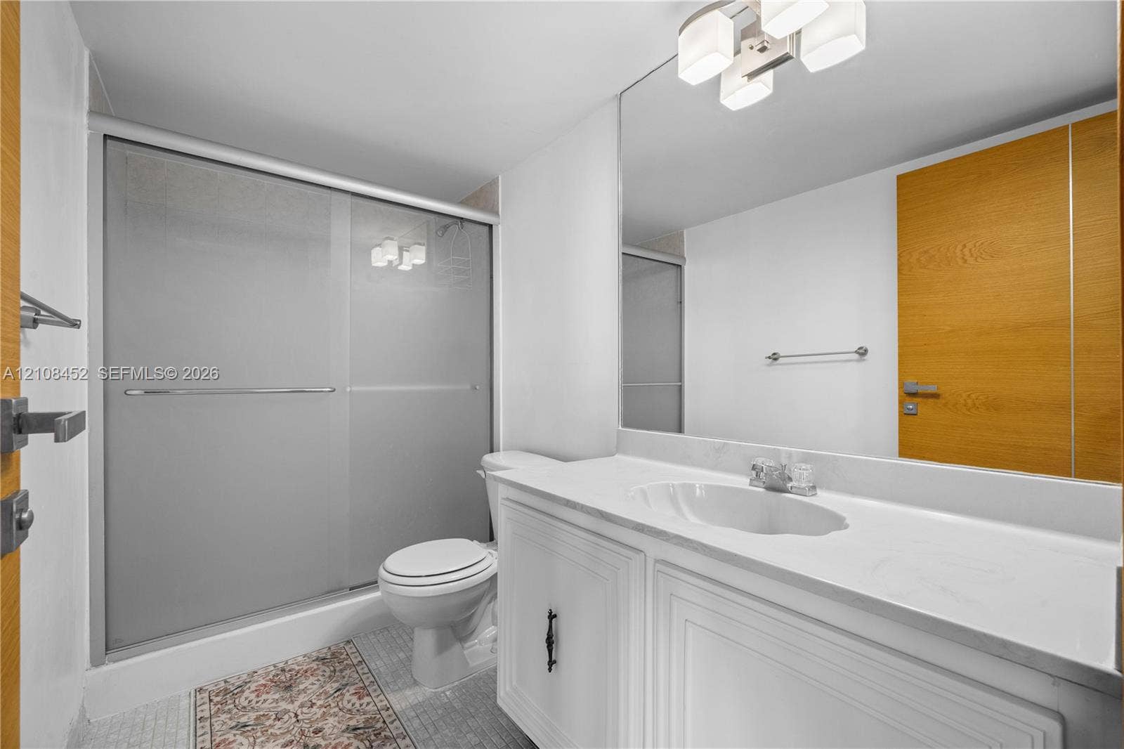 1000 Parkview Drive, #809, Hallandale Beach, FL 33009 White vanity with a stone countertop, integrated sink, large wall-mounted mirror, sliding glass shower enclosure, and modern multi-light fixture