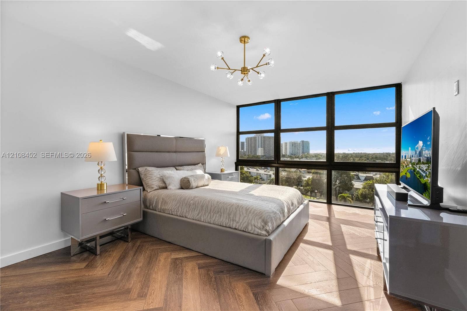 1000 Parkview Drive, #809, Hallandale Beach, FL 33009 Herringbone-pattern wood-finish flooring, floor-to-ceiling windows with panoramic exterior surroundings, and a contemporary multi-arm sputnik chandelier