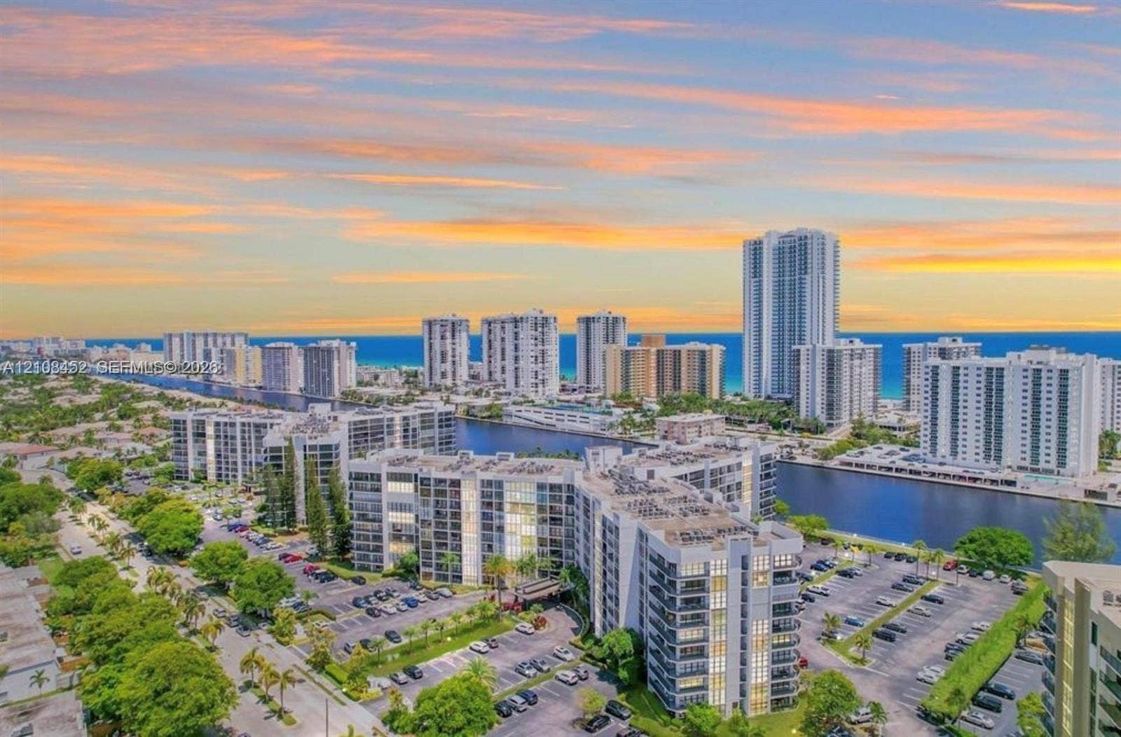 1000 Parkview Drive, #809, Hallandale Beach, FL 33009 Aerial perspective featuring multi-story residential buildings, water canal, paved parking areas, and mature landscaping against a coastal horizon