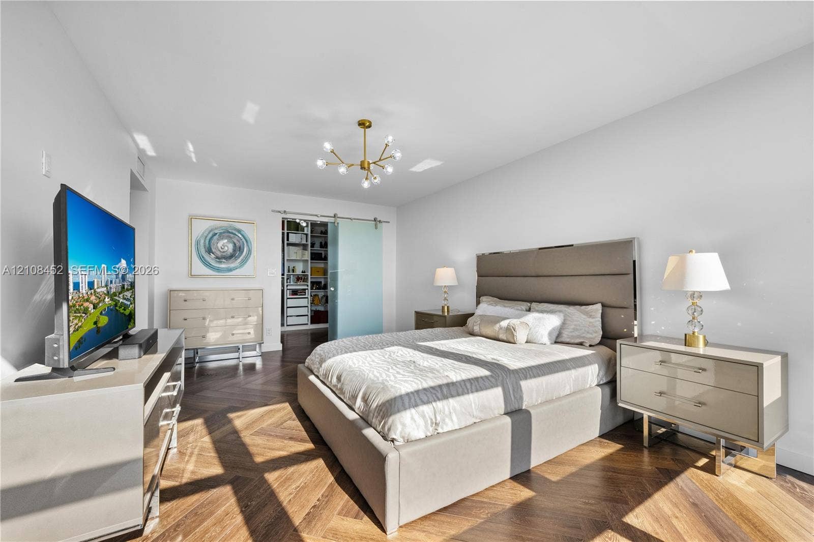 1000 Parkview Drive, #809, Hallandale Beach, FL 33009 Herringbone wood-finish flooring, gold-tone multi-arm chandelier, and frosted glass sliding door with stainless steel hardware