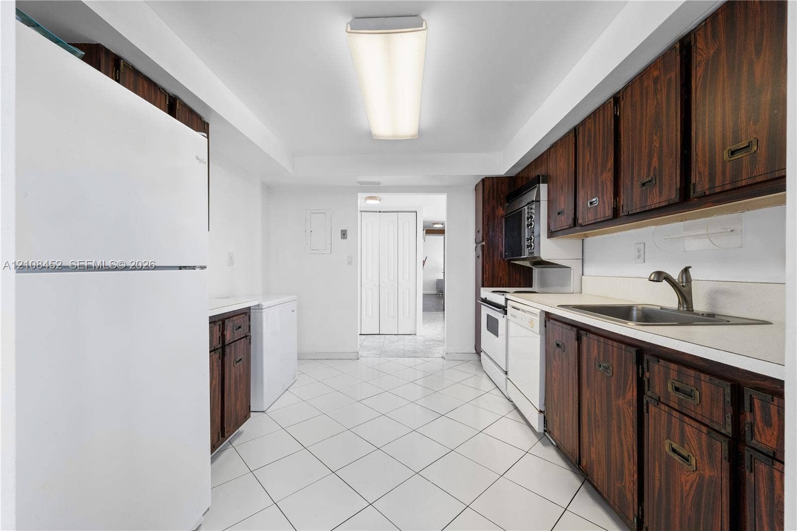 1000 Parkview Drive, #809, Hallandale Beach, FL 33009 Kitchen featuring wood-finish cabinetry, white tile flooring, integrated white appliances, and a stainless steel sink with a high-arch faucet