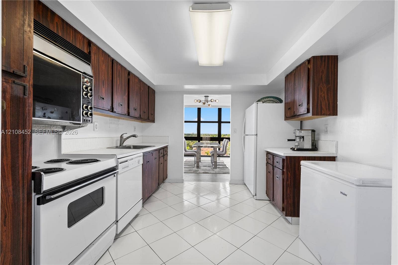 1000 Parkview Drive, #809, Hallandale Beach, FL 33009 Kitchen featuring wood-finish cabinetry, white tile flooring, integrated white appliances, and a rectangular ceiling-mounted light fixture