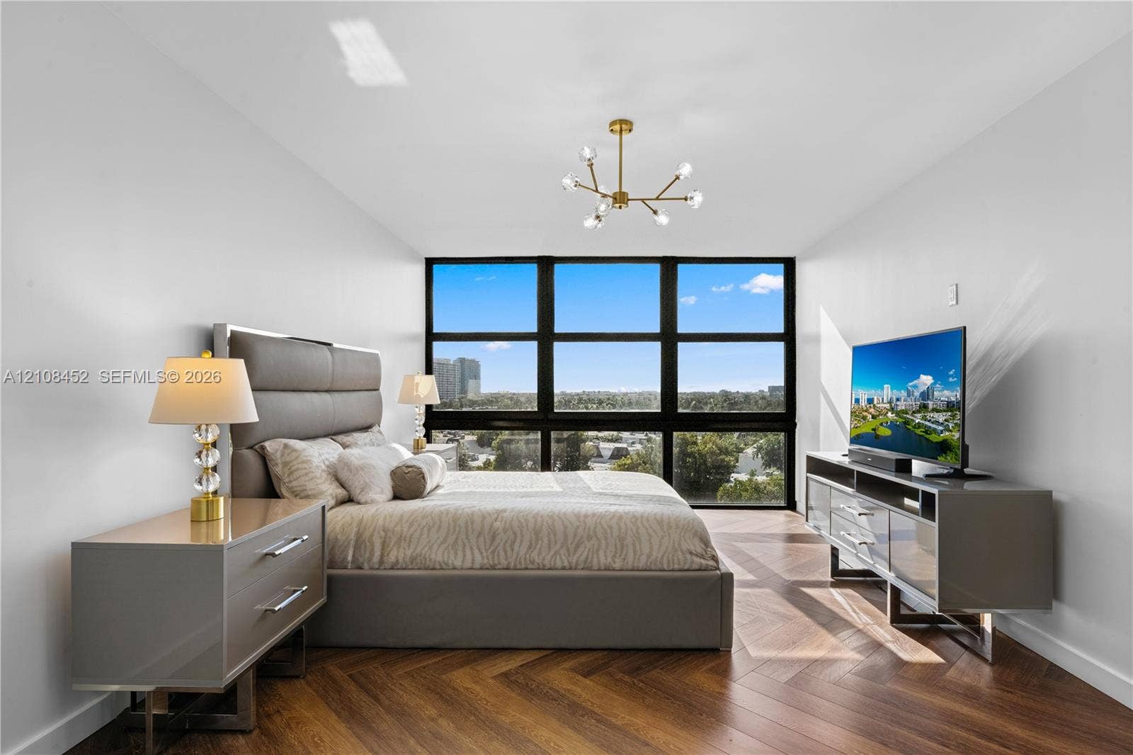 1000 Parkview Drive, #809, Hallandale Beach, FL 33009 Floor-to-ceiling windows with dark framing, wood-finish herringbone flooring, and a modern multi-arm brass chandelier