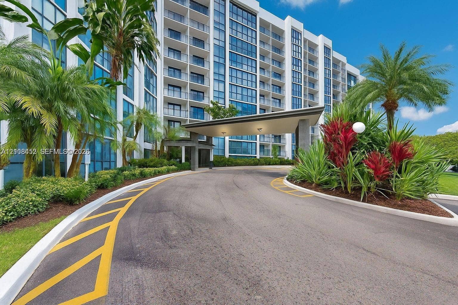 1000 Parkview Drive, #809, Hallandale Beach, FL 33009 High-rise building exterior featuring a covered porte-cochre, glass facade, expansive balcony tiers, and landscaped grounds with mature palm trees