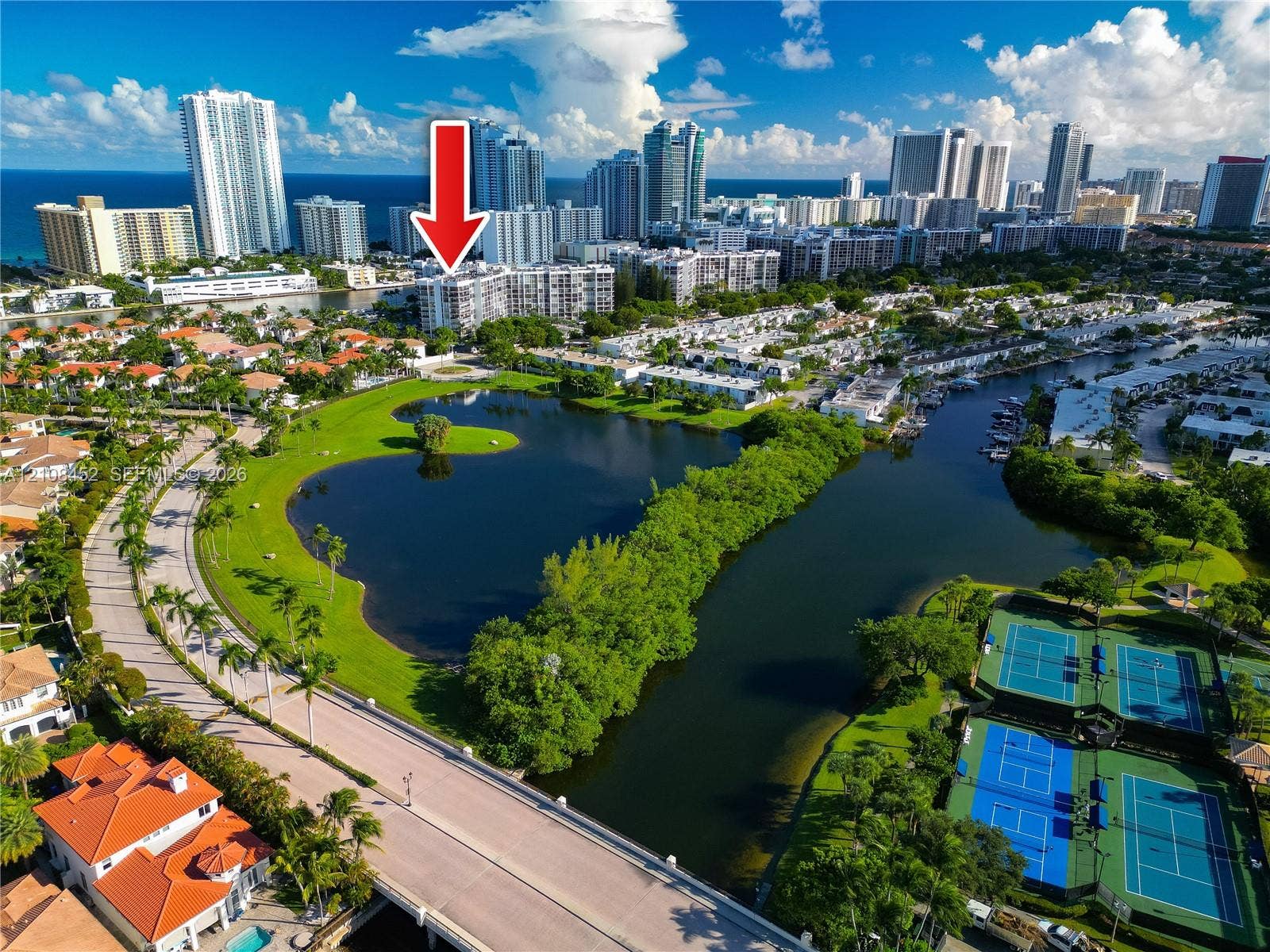 1000 Parkview Drive, #809, Hallandale Beach, FL 33009 Aerial perspective of a multi-story residential building featuring proximity to a central lake, landscaped grounds, tennis courts, and coastal waterway