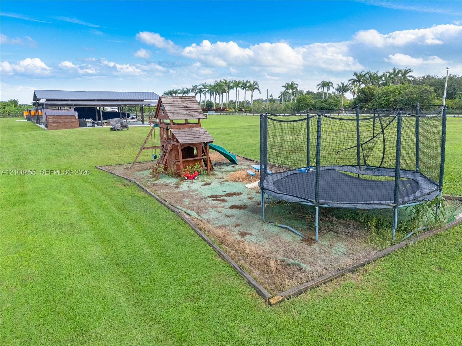 Expansive open acreage featuring a large metal-roofed pole barn and a designated area with timber-framed play structure and ground-level play surfacing