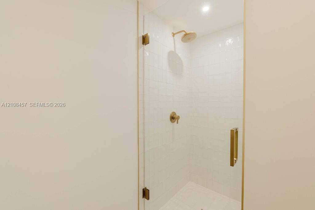 90 NE 32nd Street, #511, Miami, FL 33127 Walk-in shower featuring a frameless glass door, white wall tiling, metallic finish hardware, and a fixed shower head