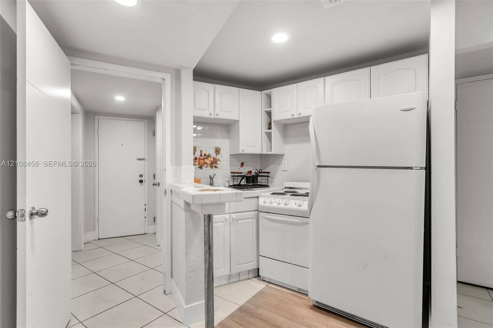 Kitchen featuring white cabinetry, a tiled breakfast bar, a white electric range, and light-toned tile flooring
