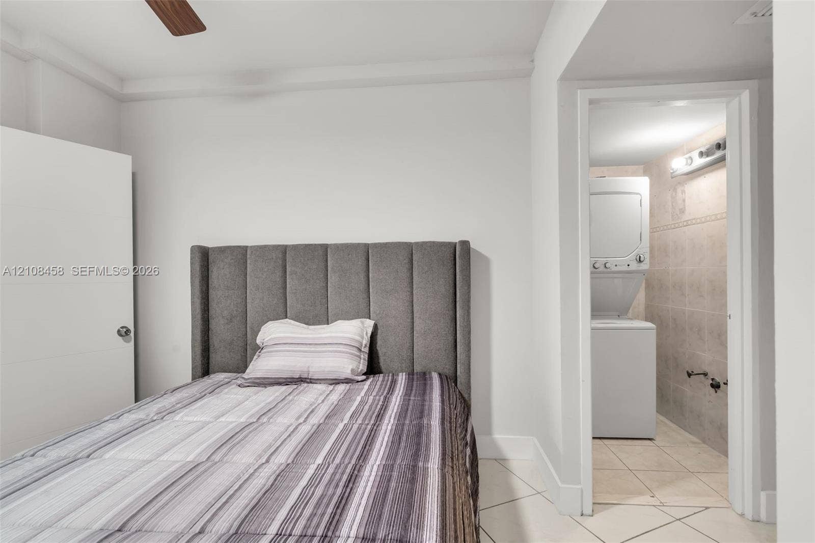 Interior space featuring white walls, tiled flooring, ceiling fan, and a dedicated laundry area with stacked washer and dryer unit