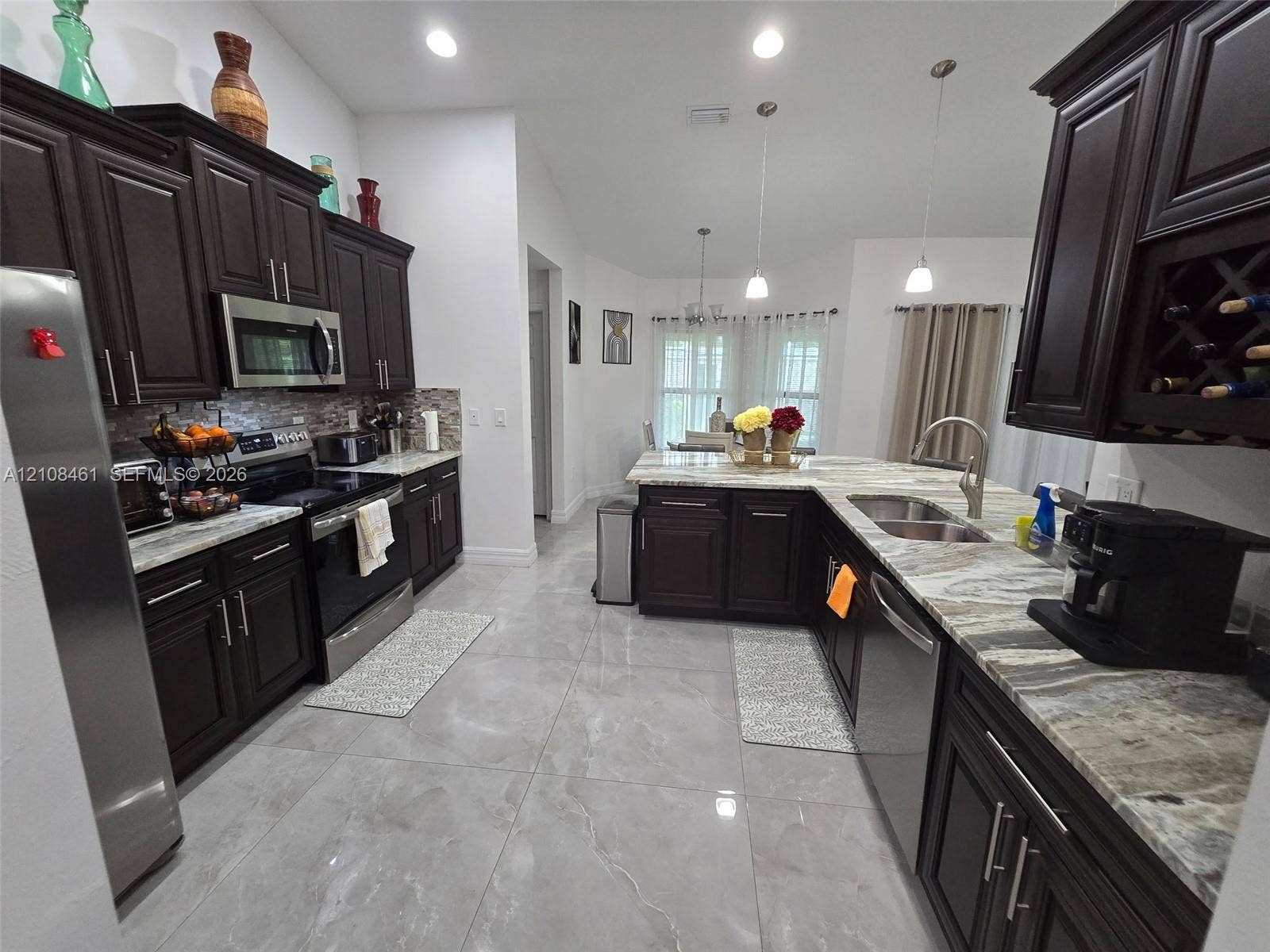 Kitchen featuring dark wood cabinetry, integrated wine storage, natural stone countertops, tile flooring, and stainless steel appliances