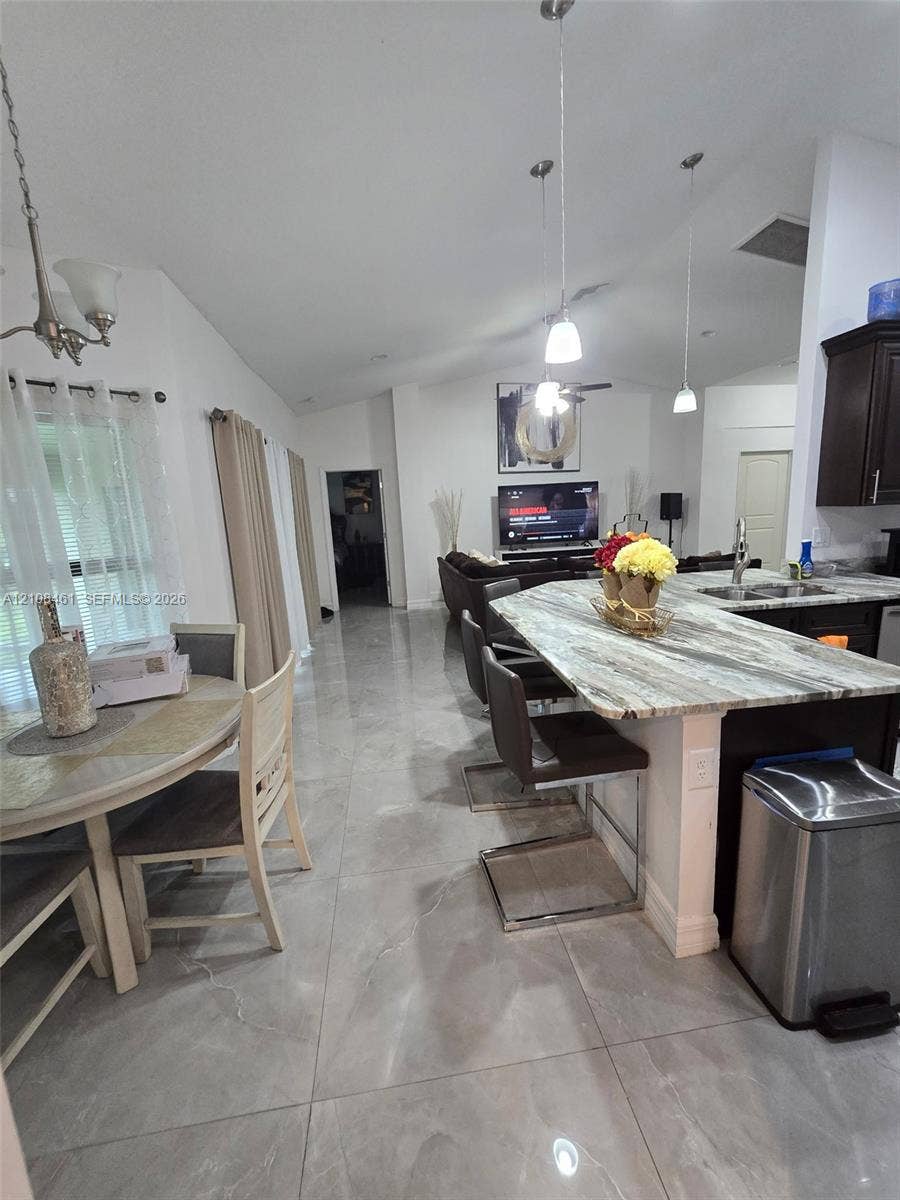 Open-concept area featuring large-format polished tile flooring, vaulted ceilings, and a kitchen island with stone-patterned countertop