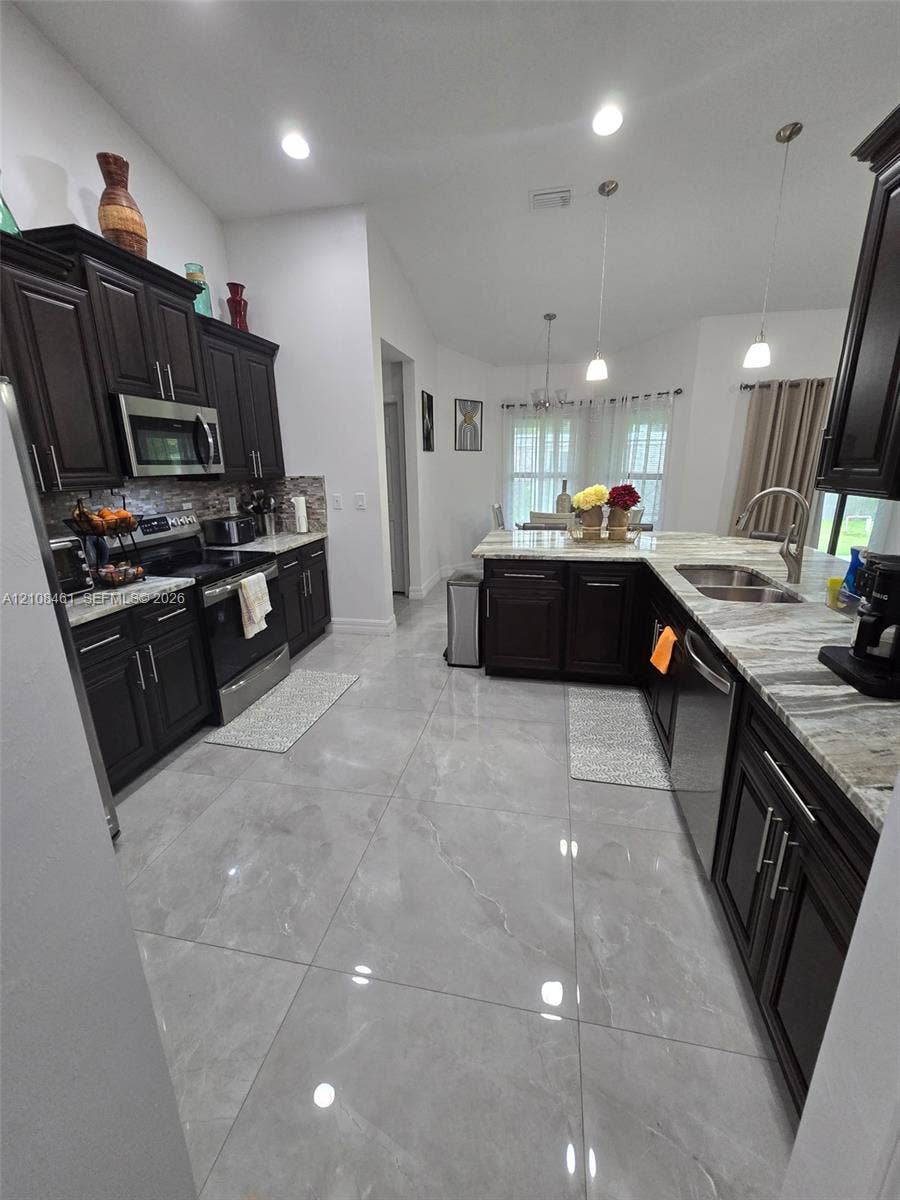Kitchen featuring dark wood cabinetry, large-format polished tile flooring, stone-finish countertops, stainless steel appliances, and pendant lighting