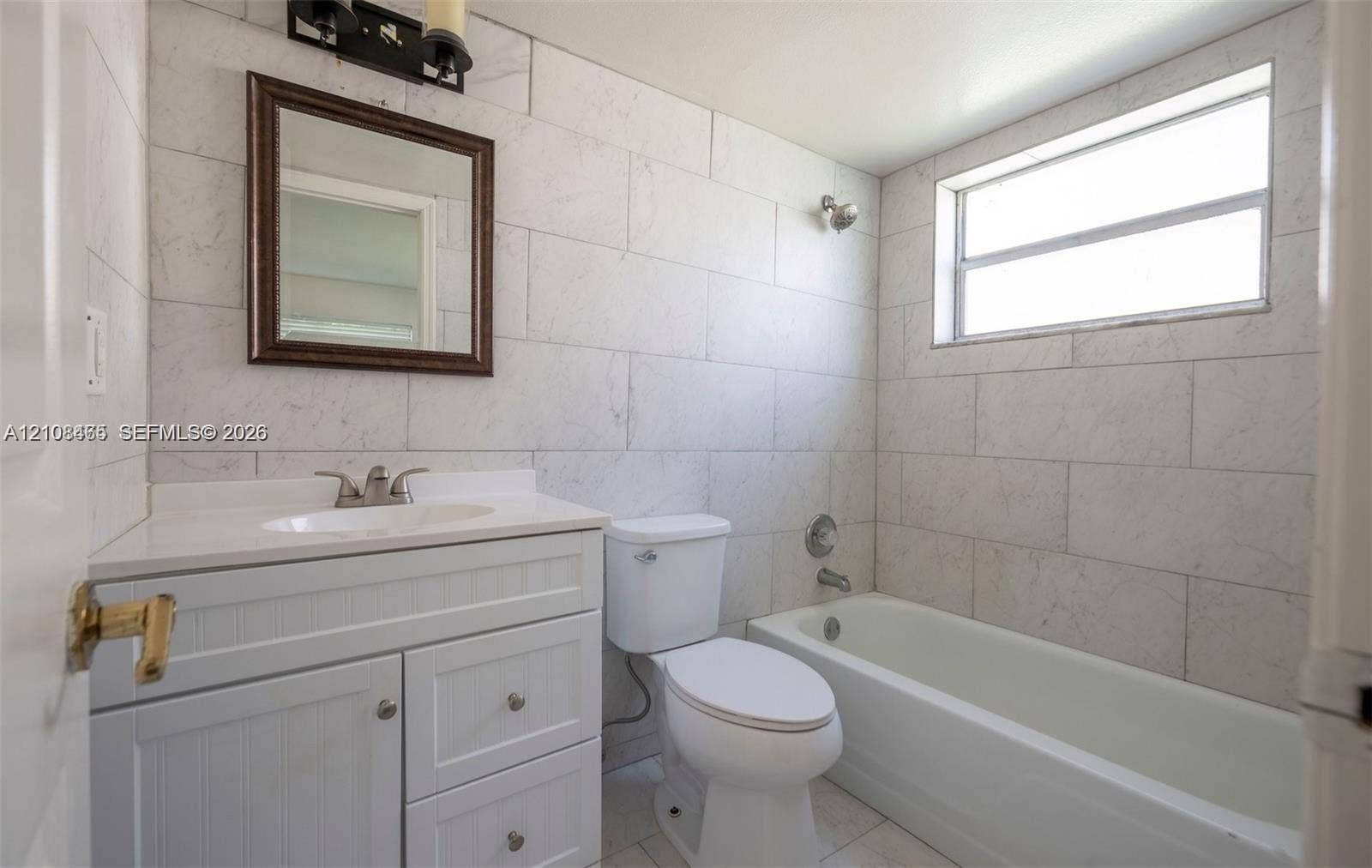 Bathroom featuring white beadboard vanity cabinetry, stone-surface countertop, full-height wall tiling, and a bathtub with a horizontal window
