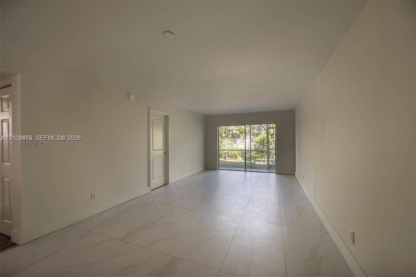 Large-format tile flooring, neutral walls, and a multi-panel sliding glass door leading to a screened enclosure