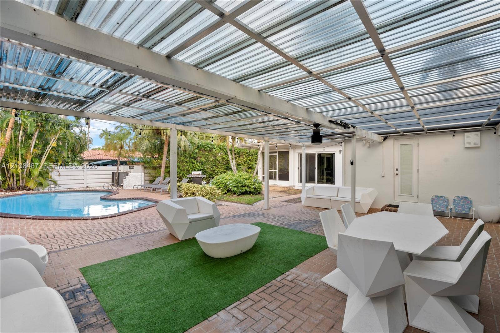Outdoor patio area featuring a semi-transparent corrugated roof, paver flooring, and an in-ground swimming pool