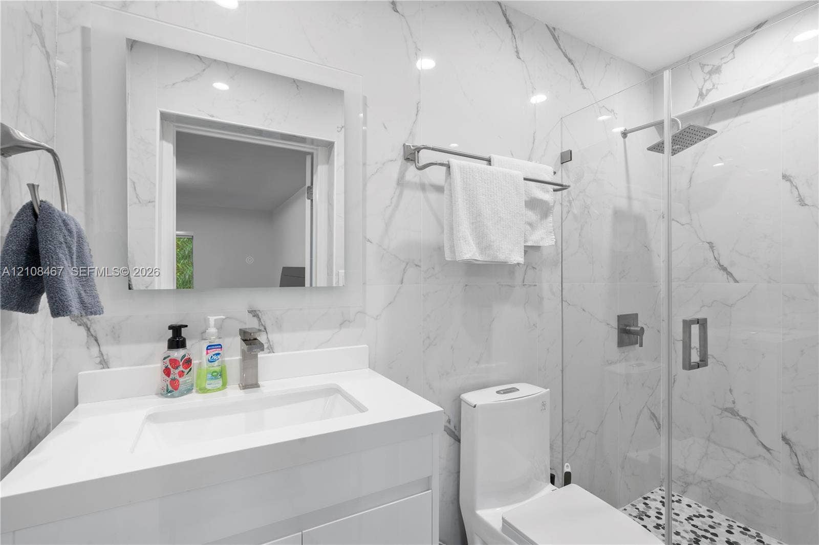 Bathroom featuring large-format wall tiling with veining detail, glass-enclosed shower with a rainfall showerhead, vanity with integrated basin, and modern polished metal fixtures