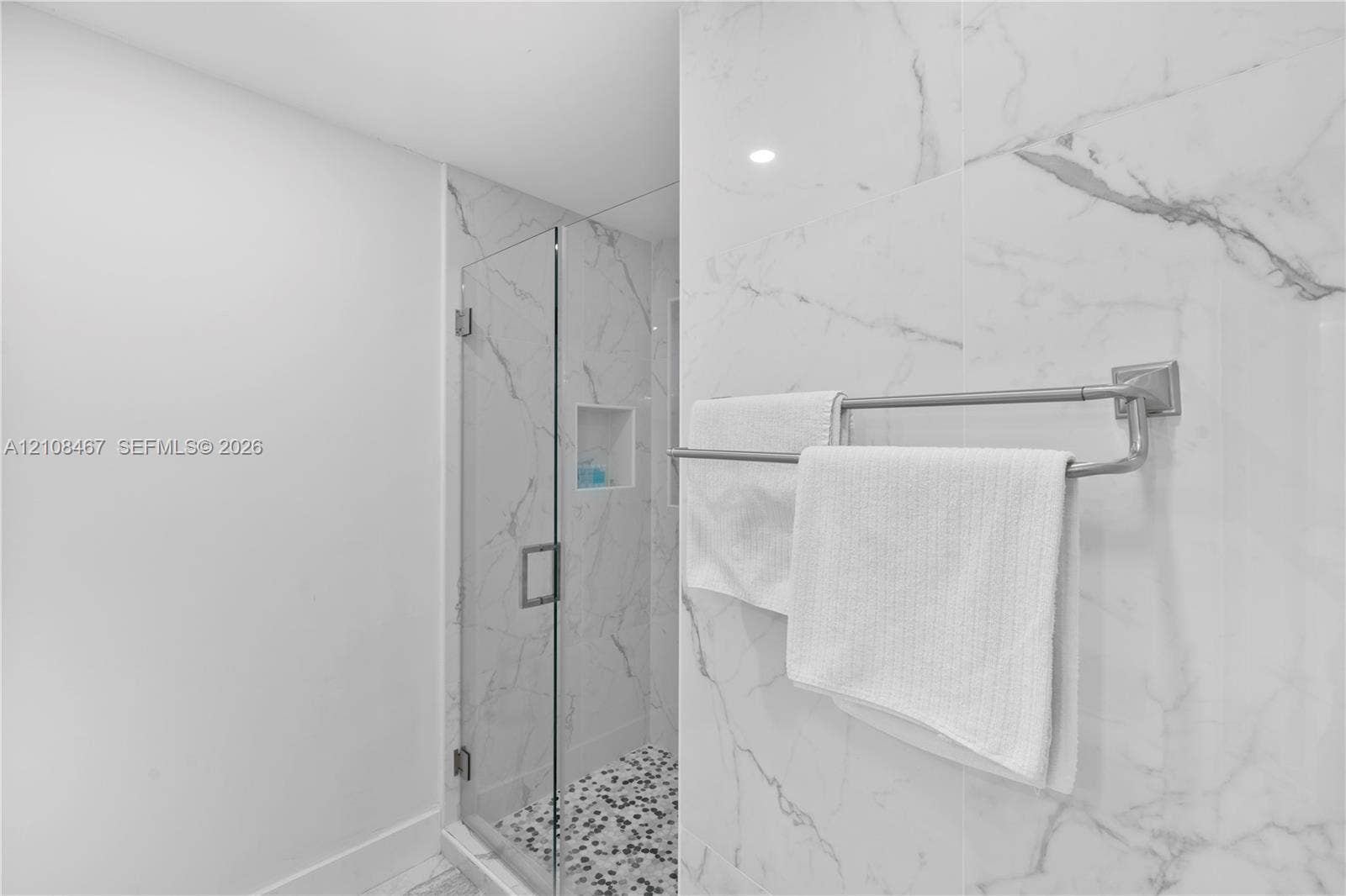 Shower featuring large-format veined wall tile, glass enclosure, built-in wall niche, and pebble-finish floor tile