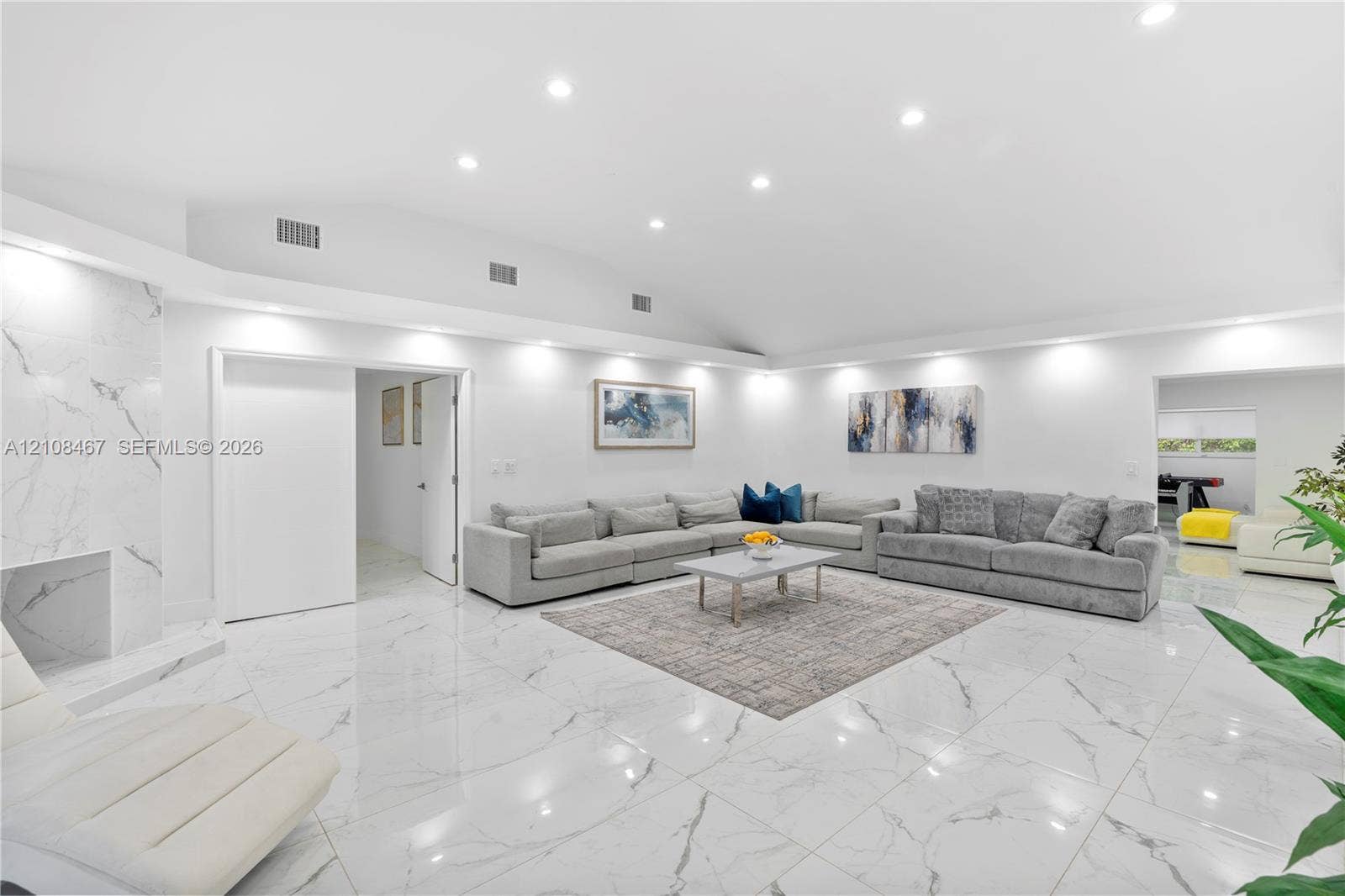Open-concept interior featuring high vaulted ceilings, large-format tile flooring with a neutral finish, and a floor-to-ceiling stone-surround fireplace