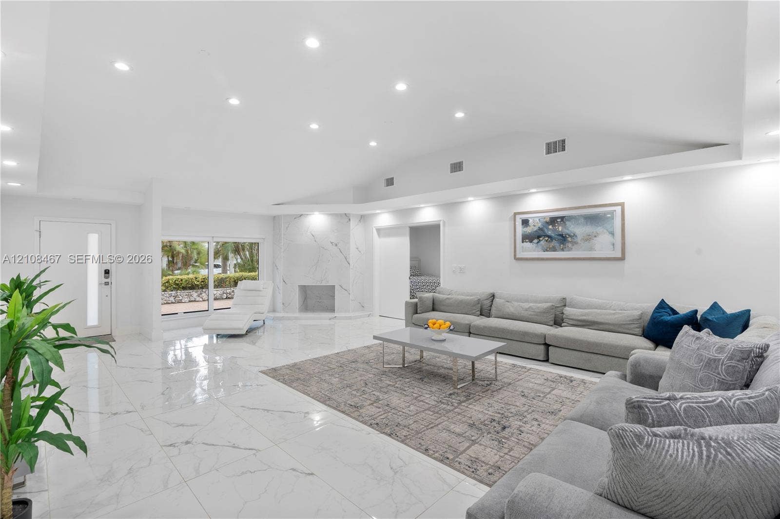 Open-concept living space featuring vaulted ceilings, polished stone-finish flooring, recessed lighting, and a floor-to-ceiling stone-surround fireplace